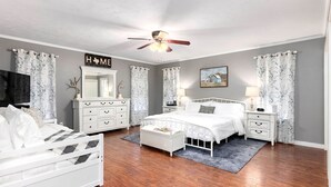 Une chambre à coucher comprenant un lit, des tables de chevet, une commode, un ventilateur de plafond et un grand miroir.