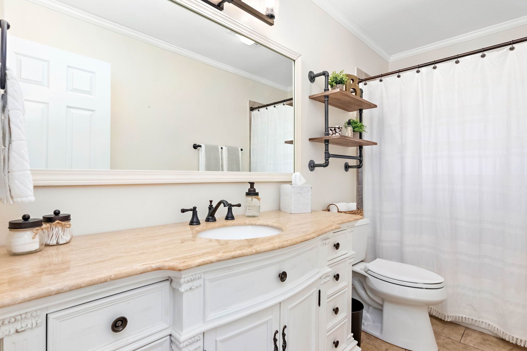 Une salle de bain avec un lavabo blanc, un grand miroir, des toilettes et un rideau de douche.
