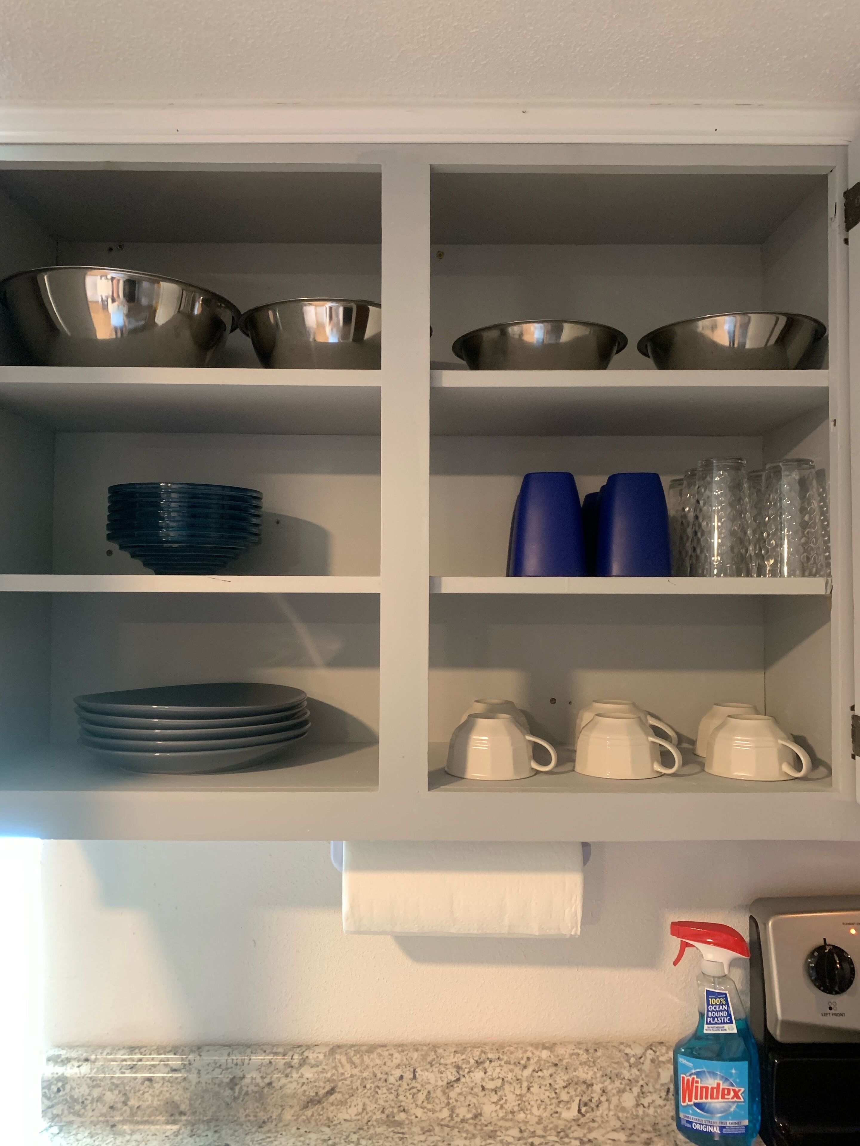 Ein Küchenschrank mit Regalen, auf denen verschiedene Küchenutensilien, darunter Schüsseln, Teller und Tassen, stehen.