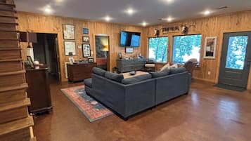 A spacious living room with a large sectional sofa, wooden walls, a mounted TV, and a staircase leading to another level.