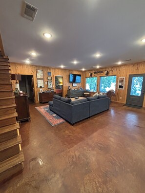 A spacious living room with a large sectional sofa, wooden walls, a mounted TV, and a staircase leading to another level.