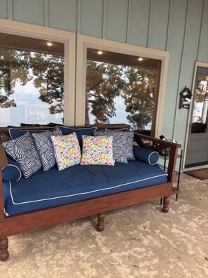 A wooden bench with a cushioned seat and backrest, positioned against a wall with large windows.