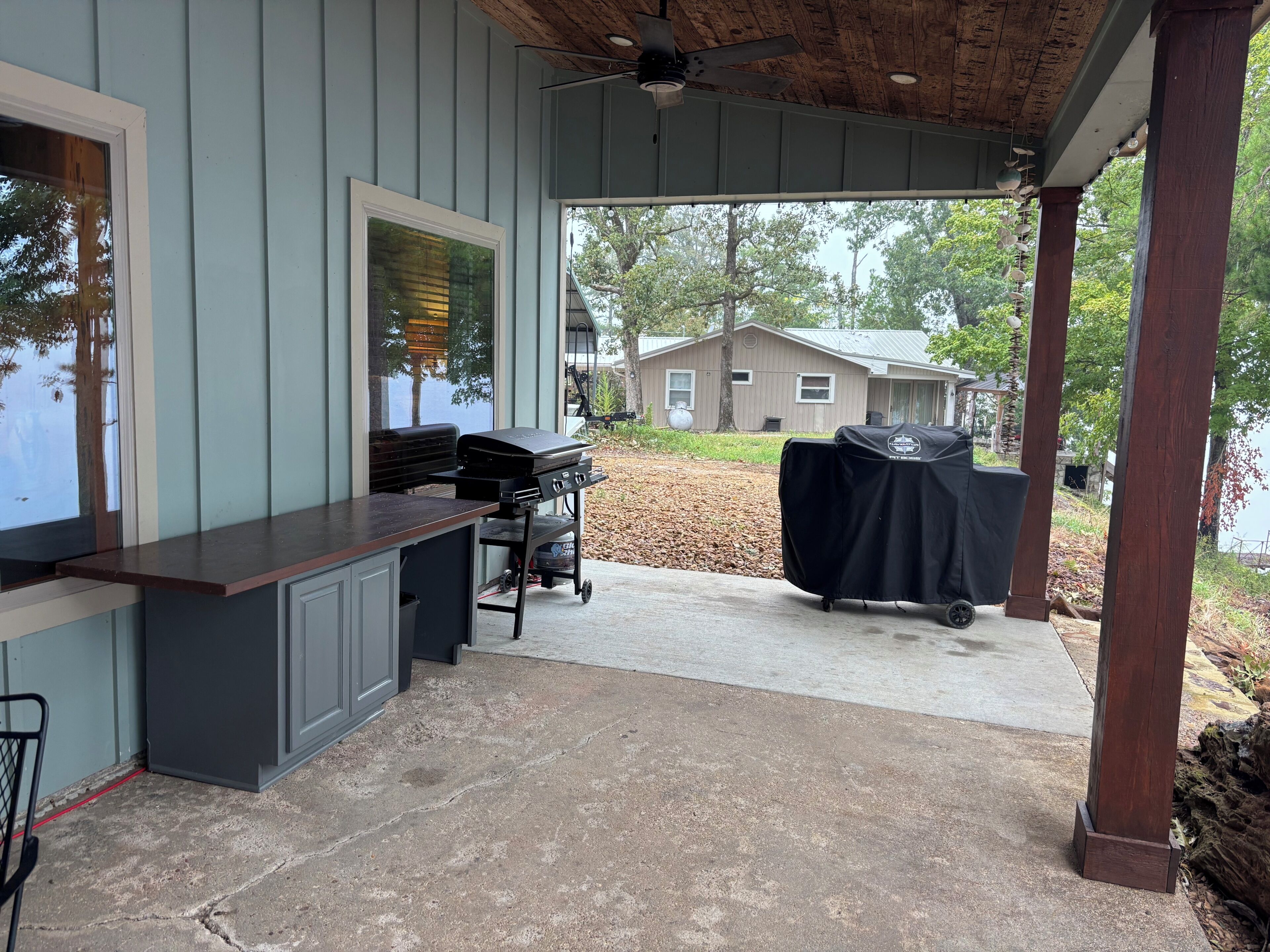 A covered outdoor area with a barbecue grill, a concrete floor, and a view of a house in the background.