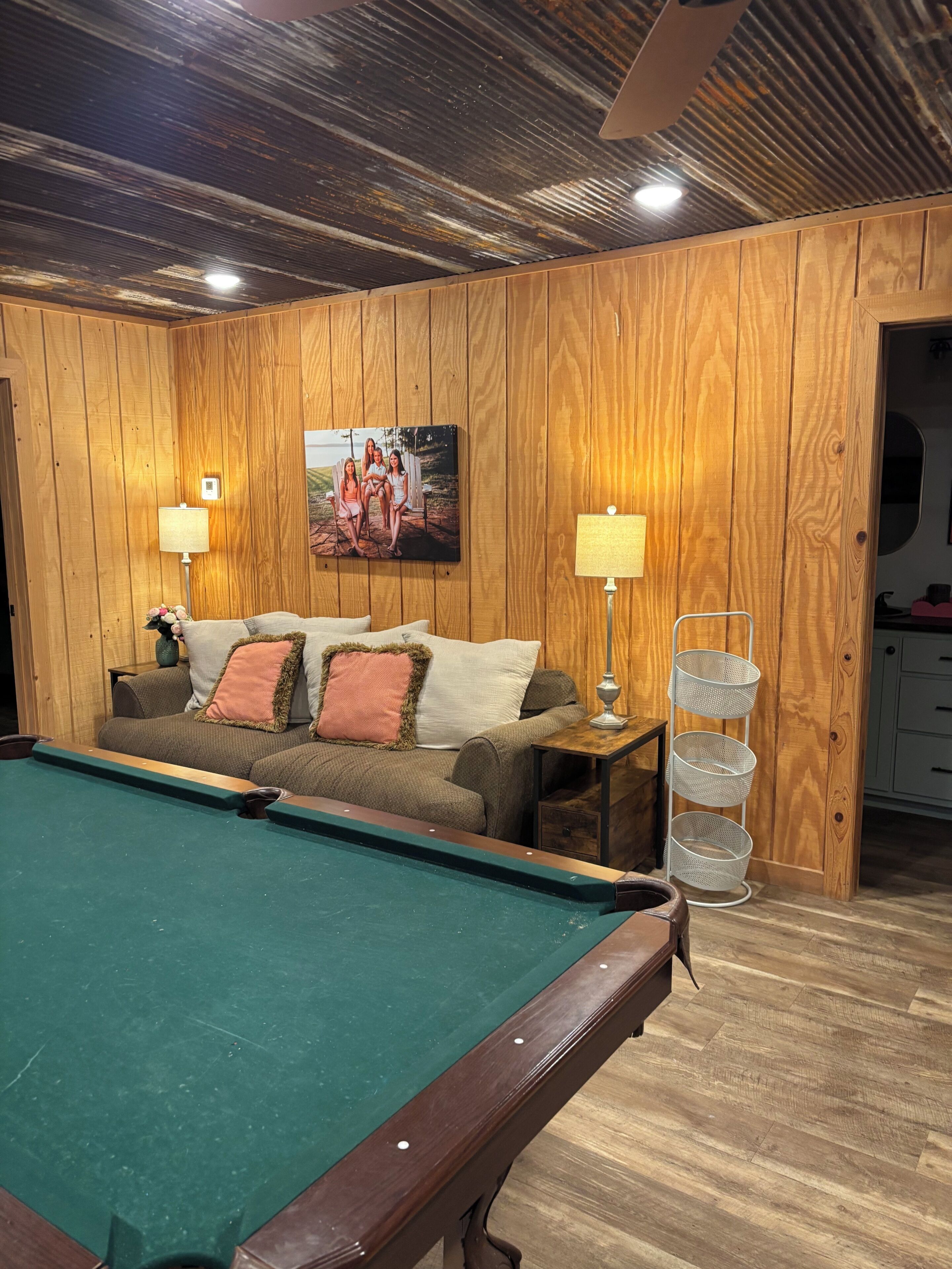 Une table de billard dans une pièce aux murs en bois, un canapé avec des coussins et une lampe.