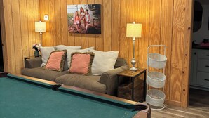 A pool table in a room with wooden walls, a sofa with cushions, and a lamp.