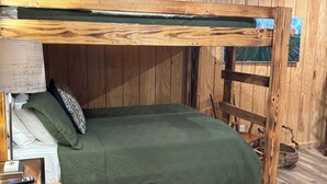 A bunk bed with a green bedspread, wooden walls, and a ceiling with exposed beams.