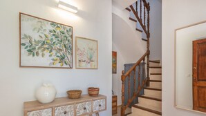 Una escalera con barandillas de madera, una consola con adornos y láminas botánicas enmarcadas en la pared.