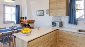 Una cocina moderna con armarios de madera, encimera blanca, microondas y comedor con mesa y sillas.