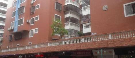 Un edificio de varios pisos con balcones, un árbol pequeño y un escaparate con señalización.