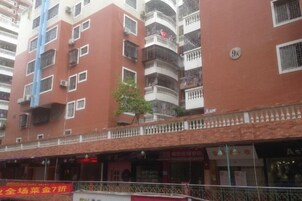 Un edificio de varios pisos con balcones, un árbol pequeño y un escaparate con señalización.