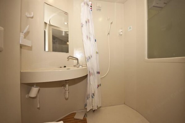 Un baño con lavamanos, espejo, ducha y dispensador de papel higiénico.