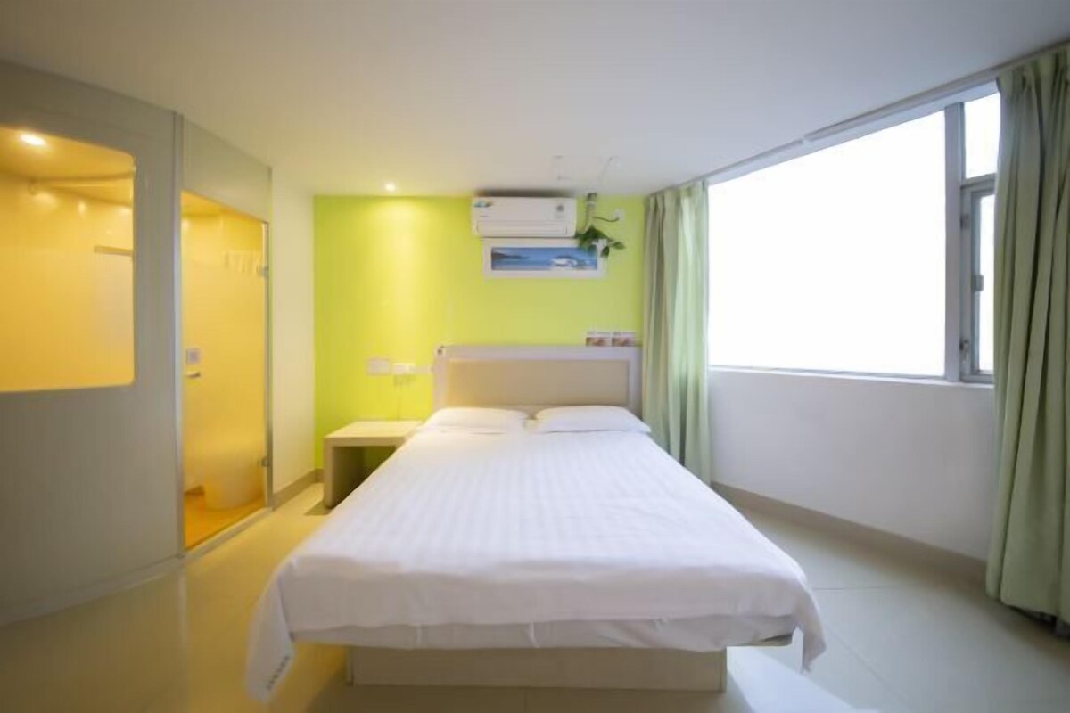 Habitación de hotel con cama, mesita de noche, aire acondicionado instalado en la pared y ventana con cortinas.