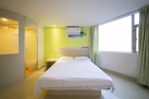 Habitación de hotel con cama, mesita de noche, aire acondicionado instalado en la pared y ventana con cortinas.