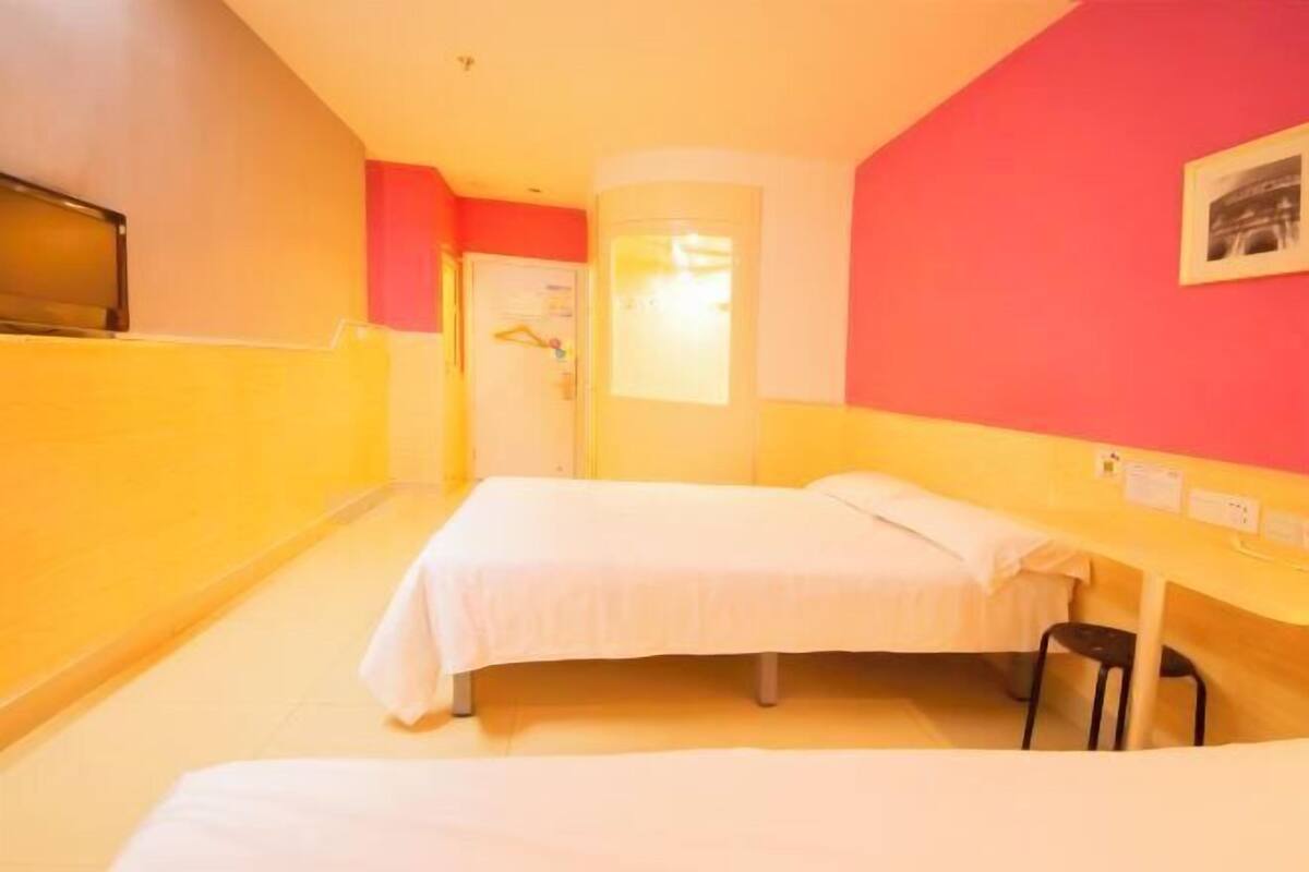 A hotel room with two beds, a desk, a chair, and a television.