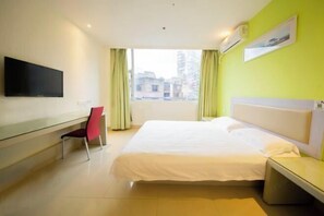 Habitación de hotel con cama, escritorio, silla, televisor y ventana con cortinas.