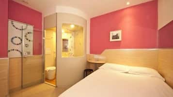 Un dormitorio con cama, una mesita, una silla, un armario y un baño visible a través de una puerta abierta.