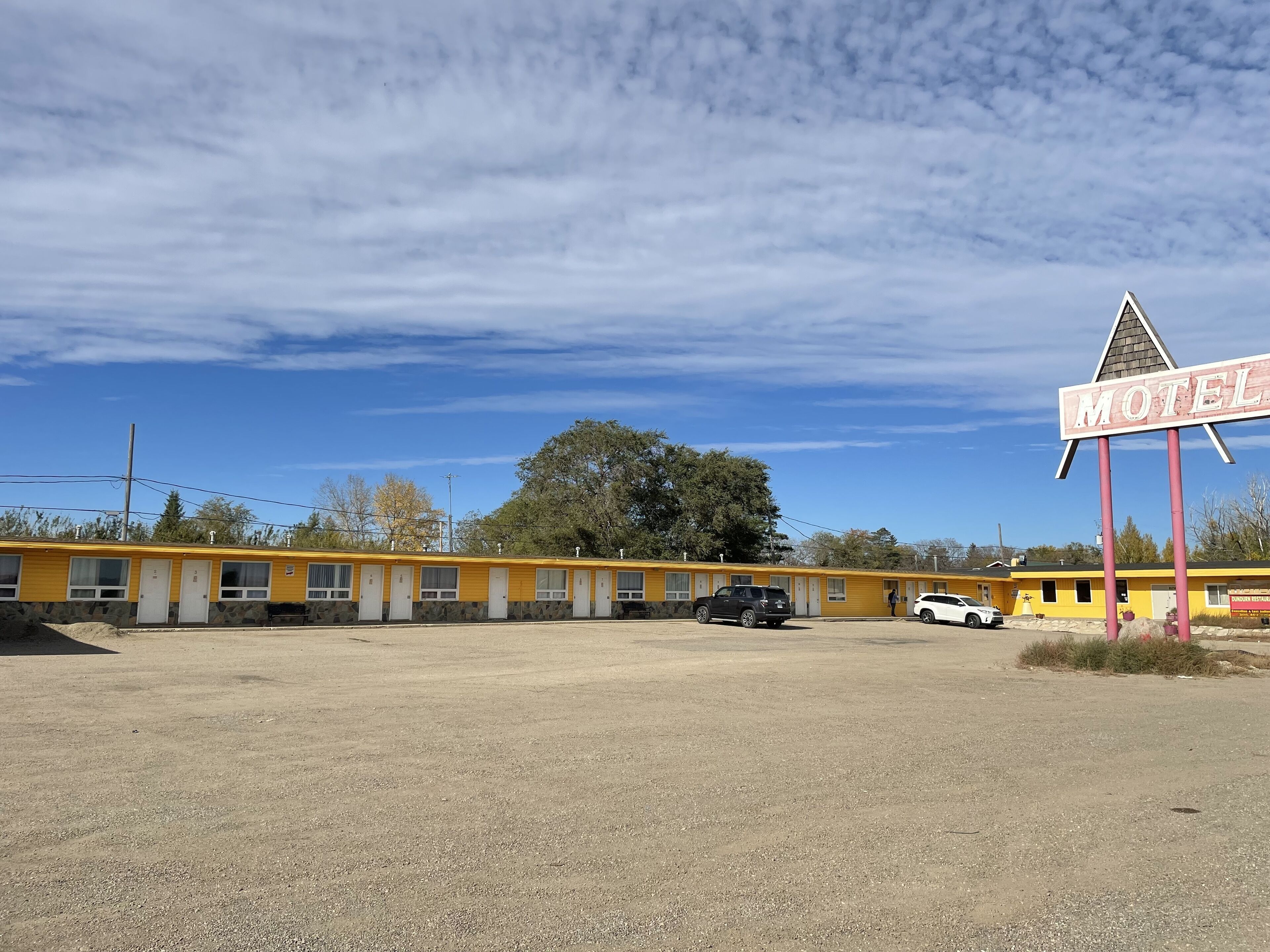 A motel with a row of single-story buildings, each with a door and windows. There is a sign indicating the motel's name.