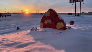 Een besneeuwd landschap met een grote rots op de voorgrond en een motelbord in de verte.