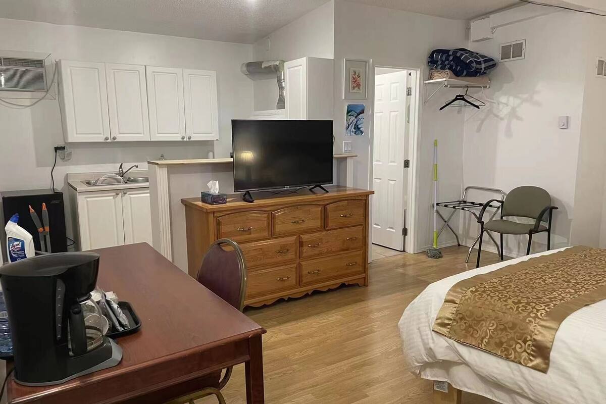 Habitación de hotel con cómoda de madera, televisor, escritorio con cafetera, cama con colcha estampada y una silla.