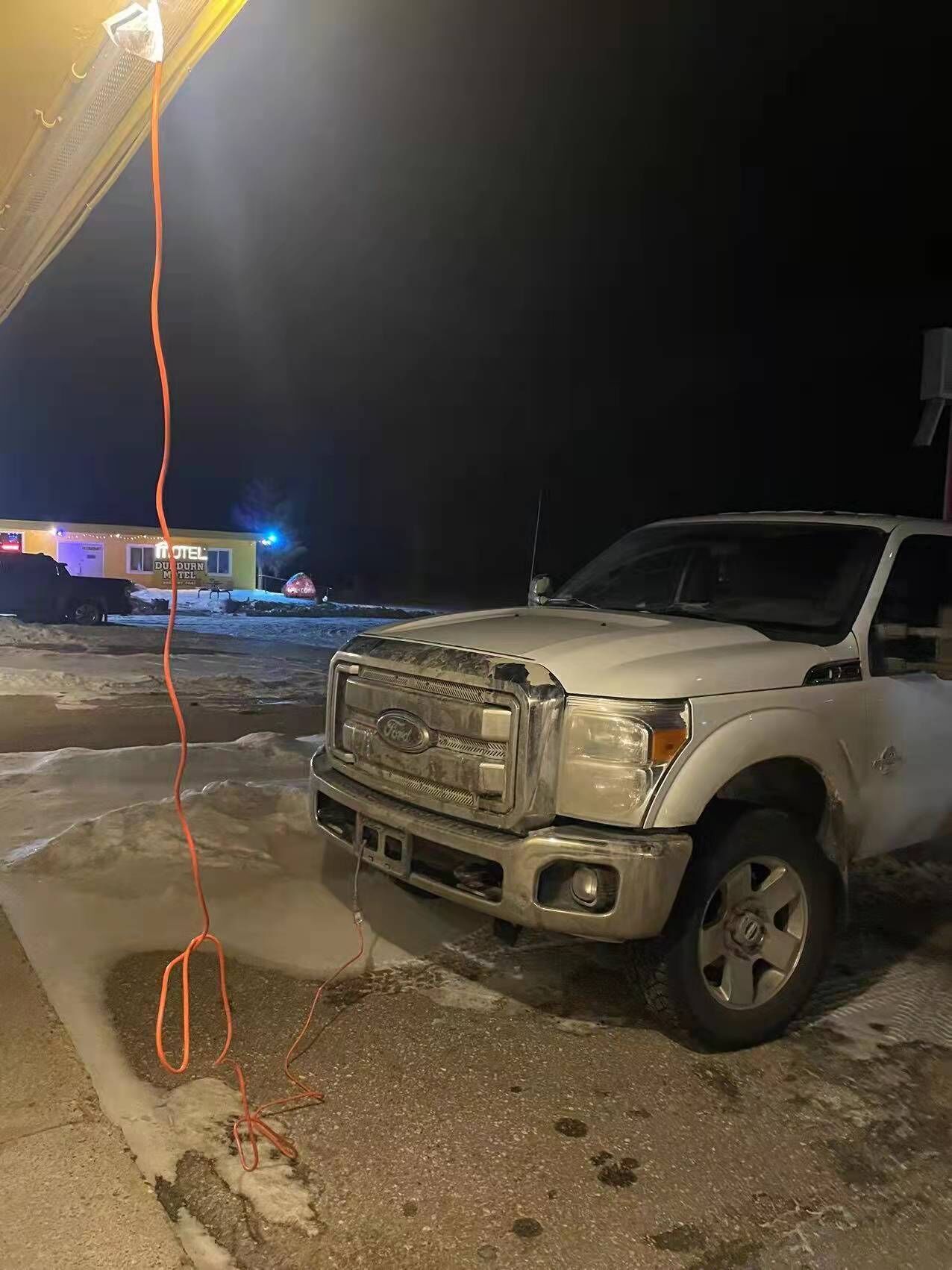Un SUV blanco estacionado en un estacionamiento, con un motel al fondo.