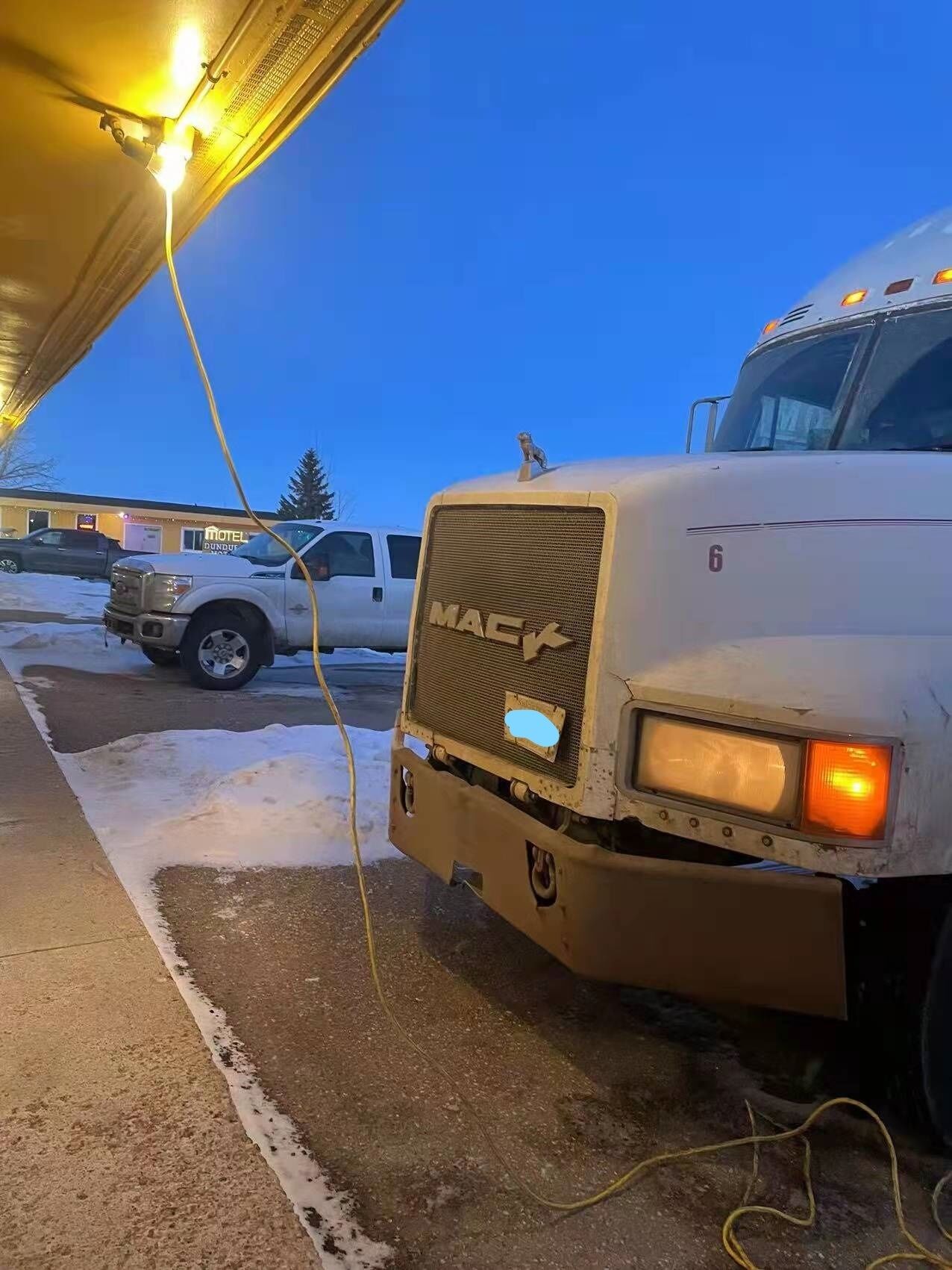 A white Mack truck parked at a motel with a visible 'Motel' sign in the background.
