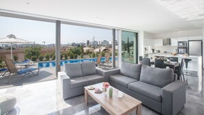 Un salón moderno con un sofá gris, una mesa de centro de madera y vistas a una piscina y al paisaje urbano.