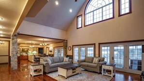 A spacious living room with a large sectional sofa, a coffee table, and a fireplace. There are large windows with multiple panes and a stone pillar. - Perfect View (Davis)