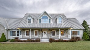 A large, two-story house with a stone facade, a metal roof, and a front porch with white railings. - Perfect View (Davis)