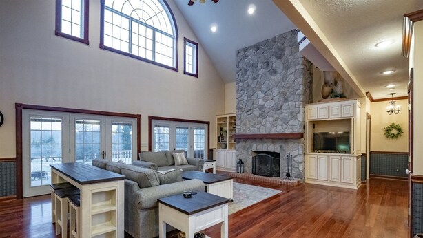 A spacious living room with a stone fireplace, wooden flooring, and a large window overlooking a snowy landscape. - Perfect View (Davis)