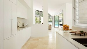 Une cuisine moderne avec des meubles blancs, une grande fenêtre et une vue sur un jardin et une piscine.
