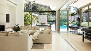 Un salon moderne doté d’une cheminée, d’un ensemble de canapés et d’une porte vitrée donnant sur un espace piscine.