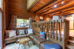 A cozy cabin interior with a wooden ceiling, a sofa set, a dining table, and a view of the outside. - The Dog House - Romantic, Hot Tub, Creekside, Firepit: Perfect couples getaway! (Boone)