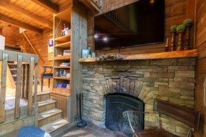 Une pièce chaleureuse avec une cheminée en pierre, des étagères en bois et un téléviseur à écran plat fixé au-dessus de la cheminée.