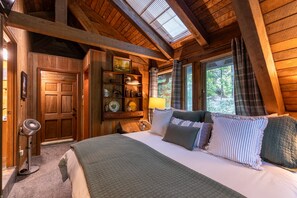 Une chambre confortable avec un plafond en bois, un lit agrémenté de plusieurs oreillers, une table de chevet et une fenêtre avec des stores.