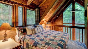 Quarto de cabana aconchegante, com uma cama grande, várias janelas e teto de madeira.