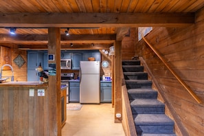 A wooden interior with a kitchen area, a staircase, and a dog figurine on the counter.