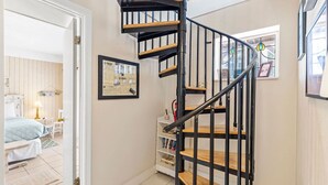 Una escalera con peldaños de madera y barandillas negras que conduce a una habitación con cama y escritorio.