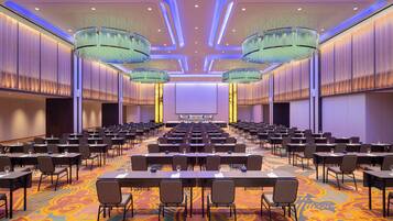 Une salle de conférence avec des rangées de tables et de chaises, un grand écran à l’avant et un éclairage moderne.