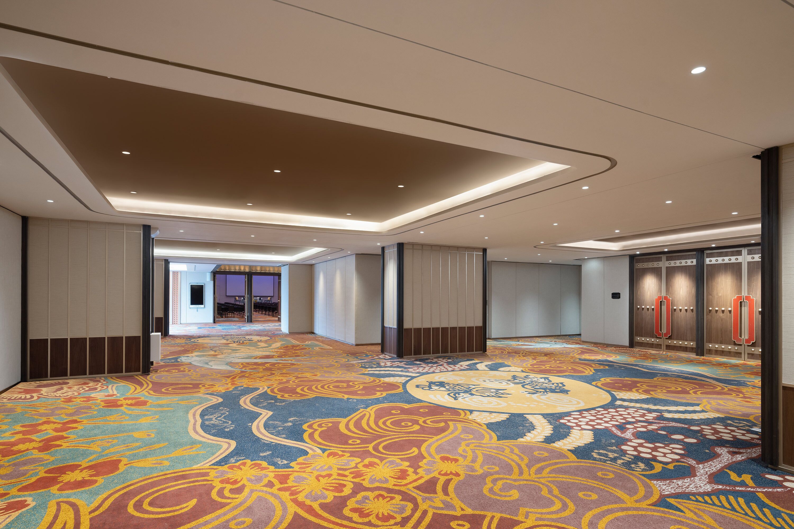 A hotel corridor with patterned carpet, recessed lighting, and wooden lockers.