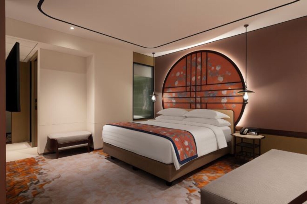 A modern hotel room with a large bed, a bedside table, a nightstand, and a wall-mounted TV.