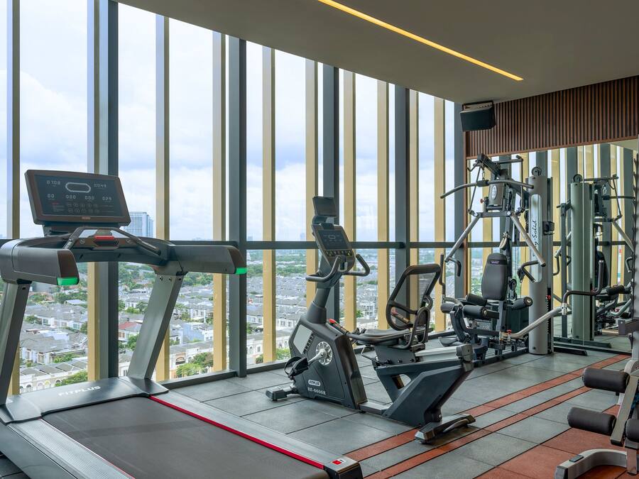 A gym with a treadmill, elliptical, and weight machines, large windows with a city view.