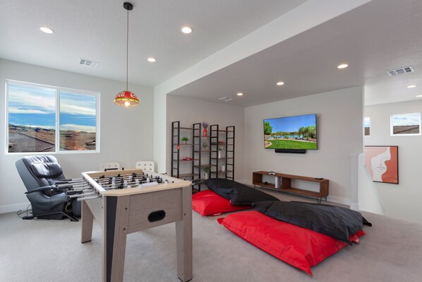 A modern room with a foosball table, a sofa, a TV, and a window with a view of a landscape. - Paseos 1129 | Foosball Table, BBQ Grill, Xbox S, Community Trailer Parking & Pickleball Courts! (Washington)