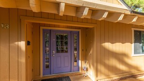 Une maison en bois avec une porte violette, une plaque portant le numéro « 13 » et un petit porche.