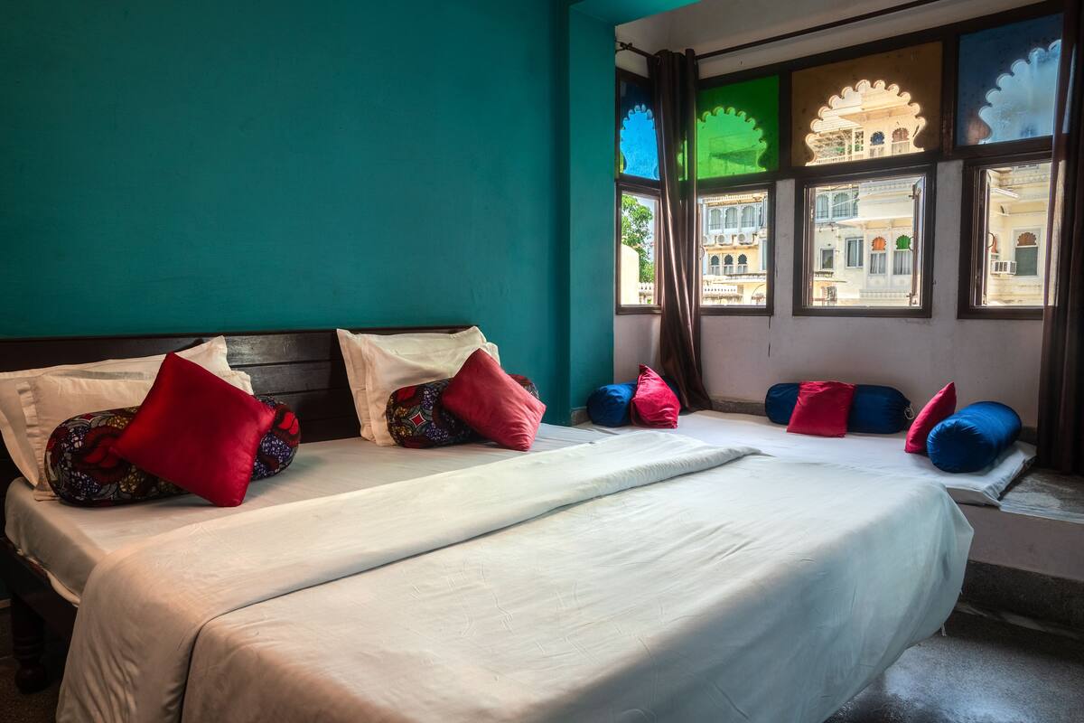 A hotel room with two beds, teal walls, and windows with traditional architectural views.
