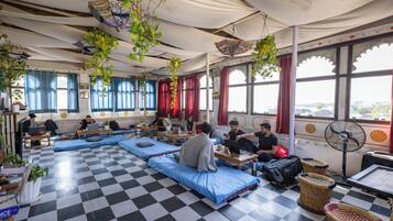 Una habitación con suelo de cuadros, asientos acolchados azules, plantas colgantes y ventanas grandes con cortinas rojas.