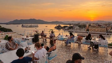 A terrace with tables and chairs overlooking a body of water and a sunset.