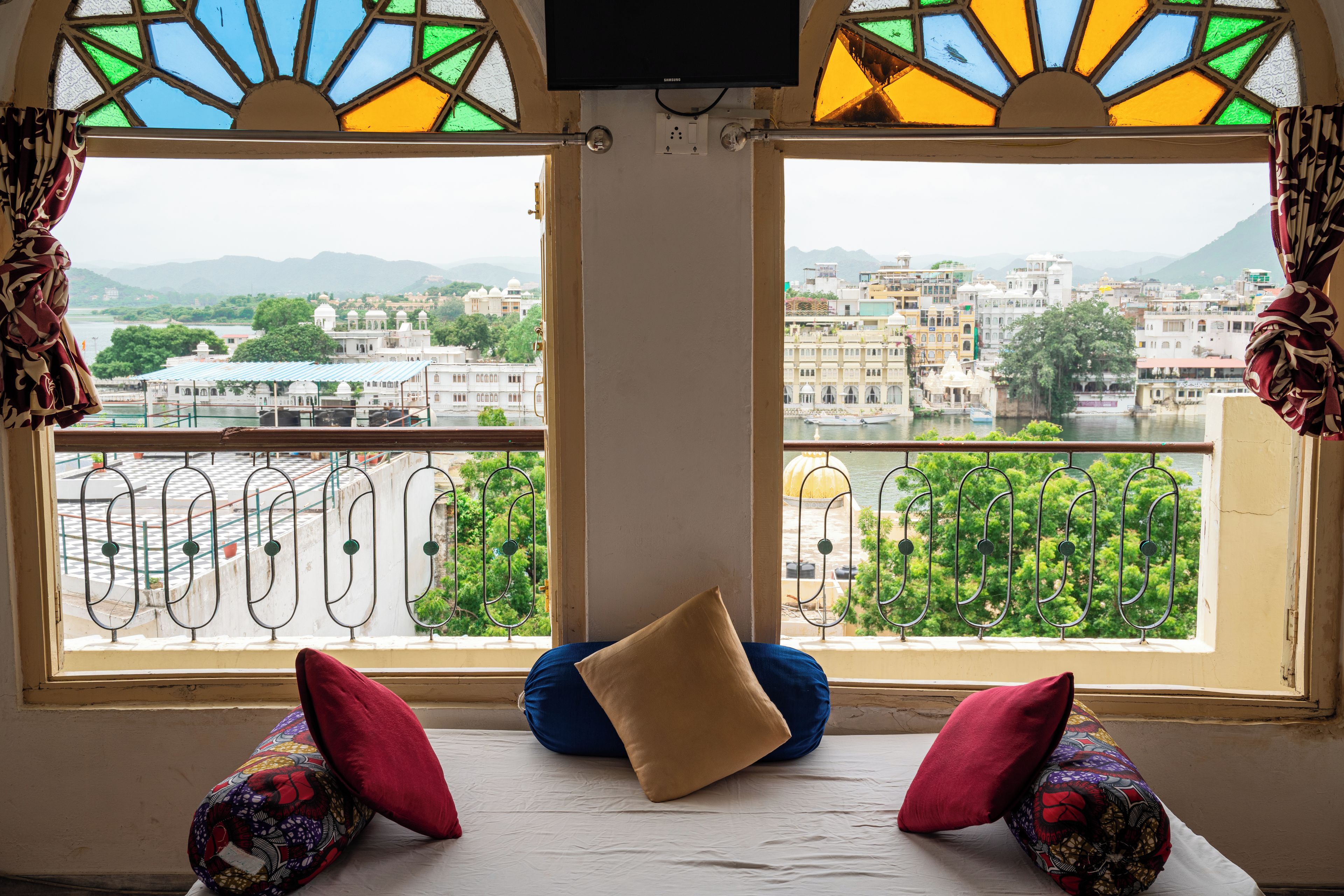 A room with a bed, two pillows, and a view of a cityscape through a window with stained glass.