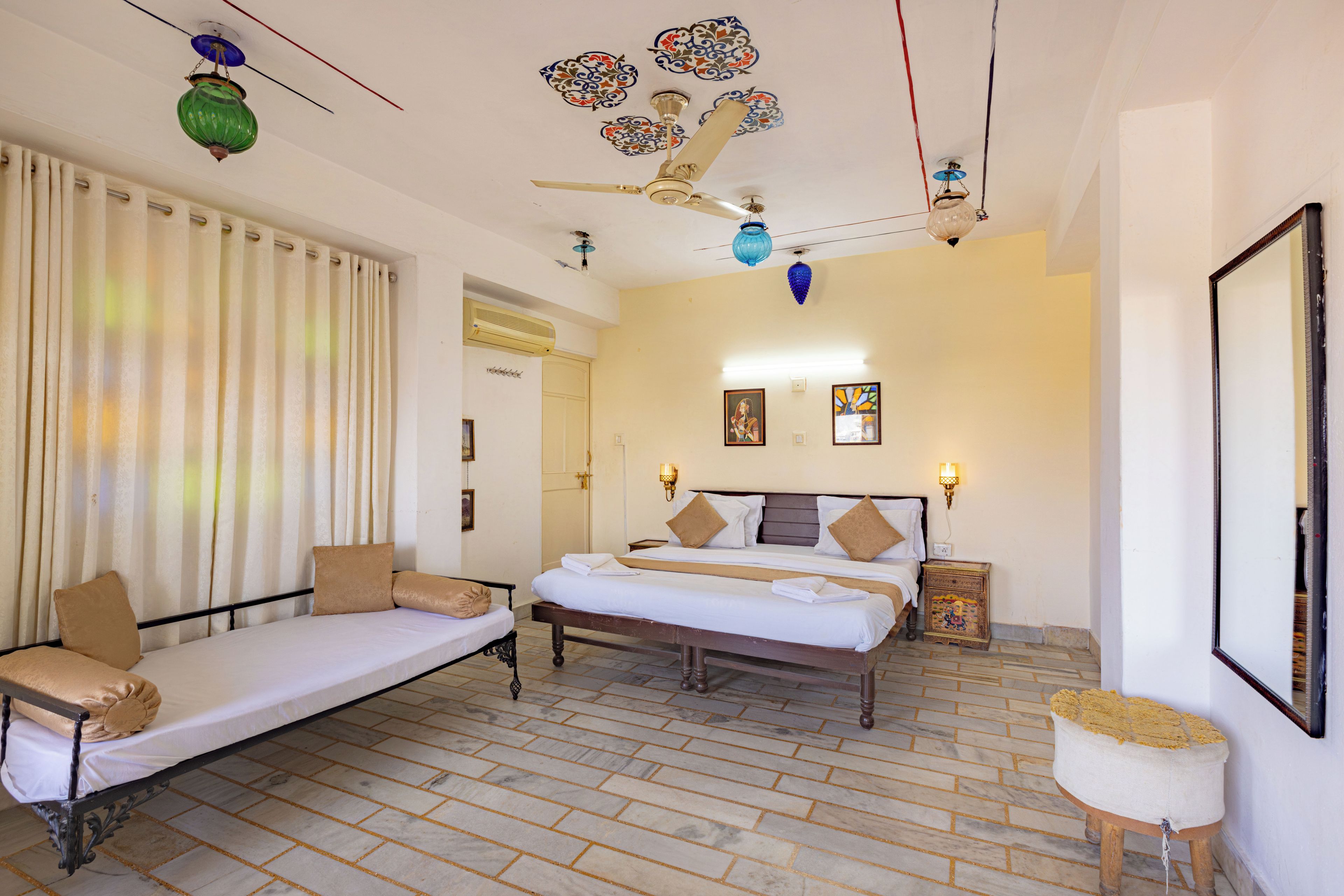 A room with a bed, a sofa, a small table, and a decorative ceiling.