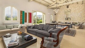 Un vaste espace de vie comprenant un grand canapé, une table basse avec des livres, une cheminée et un mur en pierre.