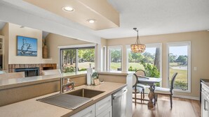 Una cocina con una isla grande, un comedor con mesa y sillas, y ventanas amplias que ofrecen vistas al exterior.
